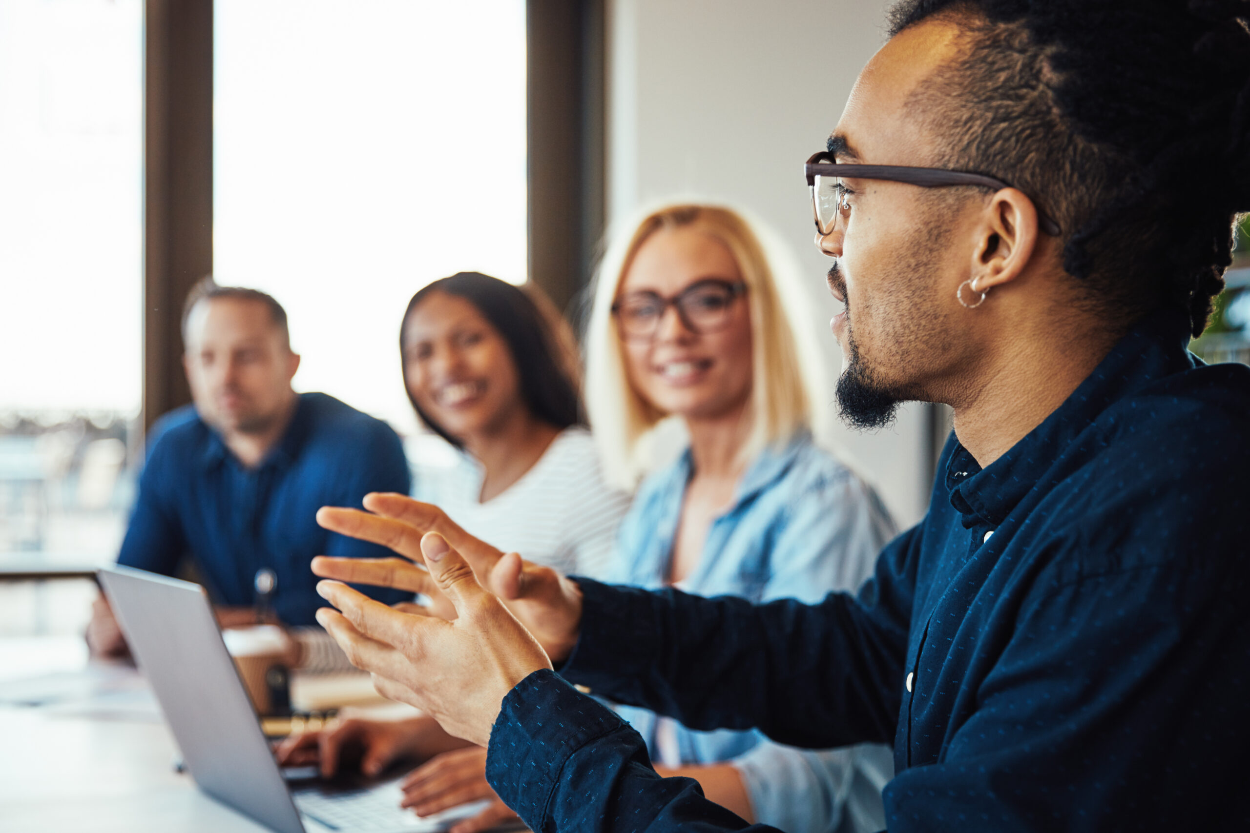 Smiling young African American businessman discussing work with a diverse group of colleagues sitting together at an office table